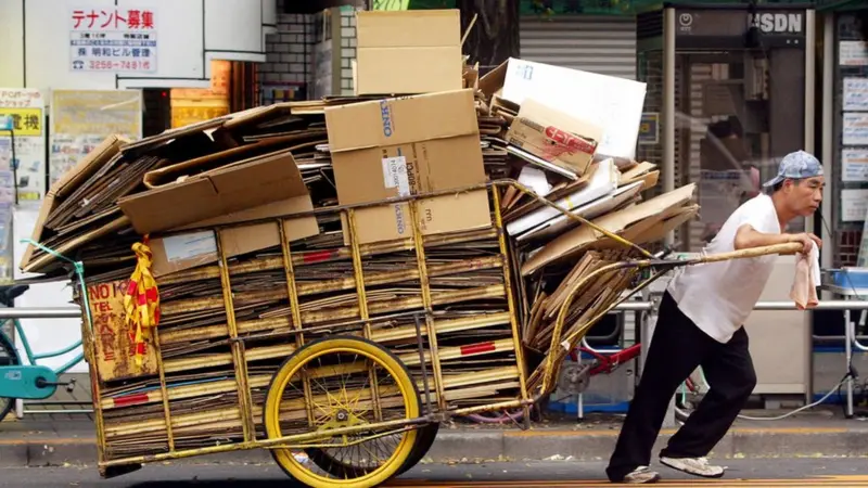 Trabajador japonés transportando cartón reciclado en un carro, muestra de la economía circular y del respeto a los recursos.